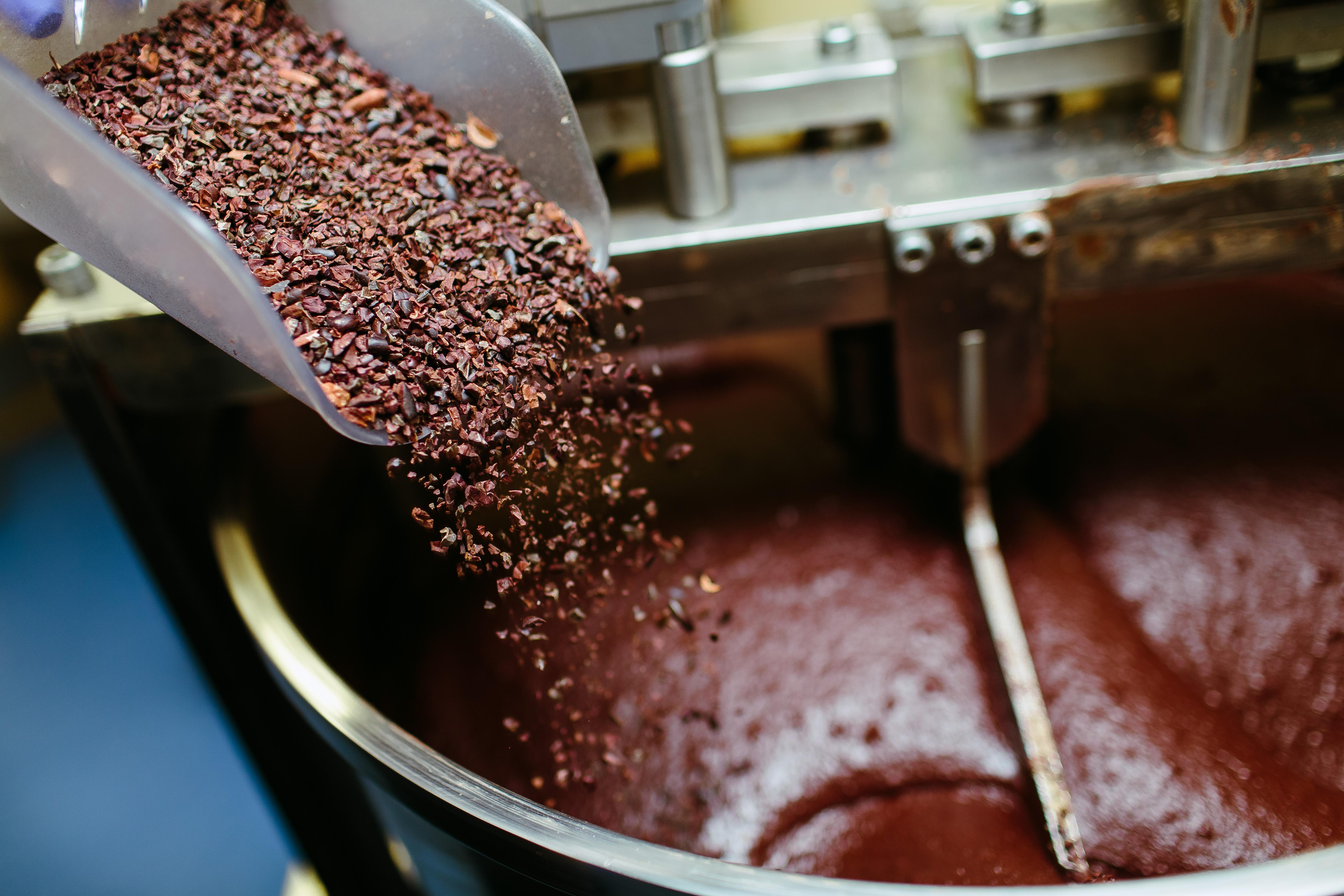 Cocoa grits being poured into a grinder full of chocolate